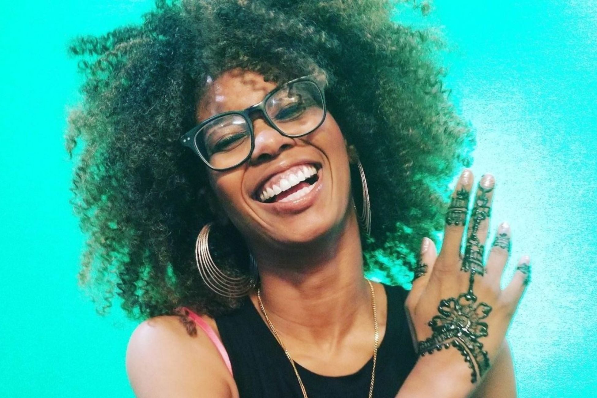 A woman joyfully smiles and displays a detailed henna tattoo on her hand.