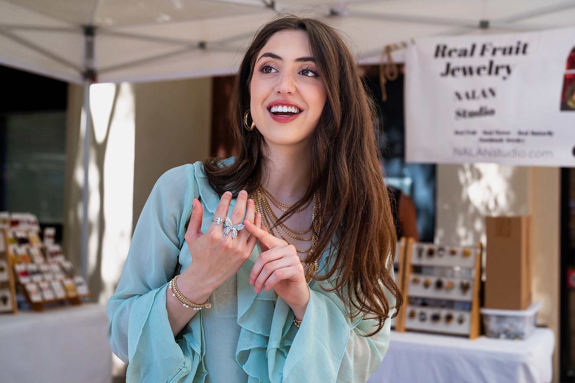 A young woman wearing gold jewelry and a light blue blouse smiles while standing at an outdoor market booth. Large white text across the image reads “story of connection.”